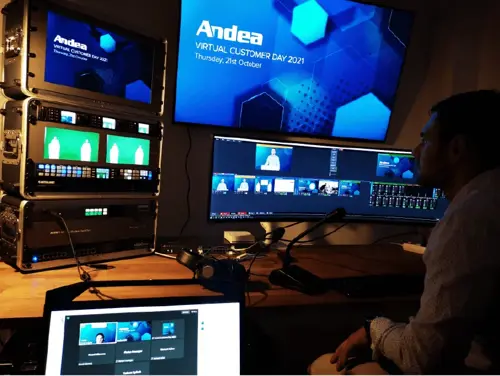 A man is overseeing a live broadcast production for Andea's Virtual Customer Day 2021. Multiple monitors display production feeds, software interfaces, and event branding, highlighting manufacturing software solutions.